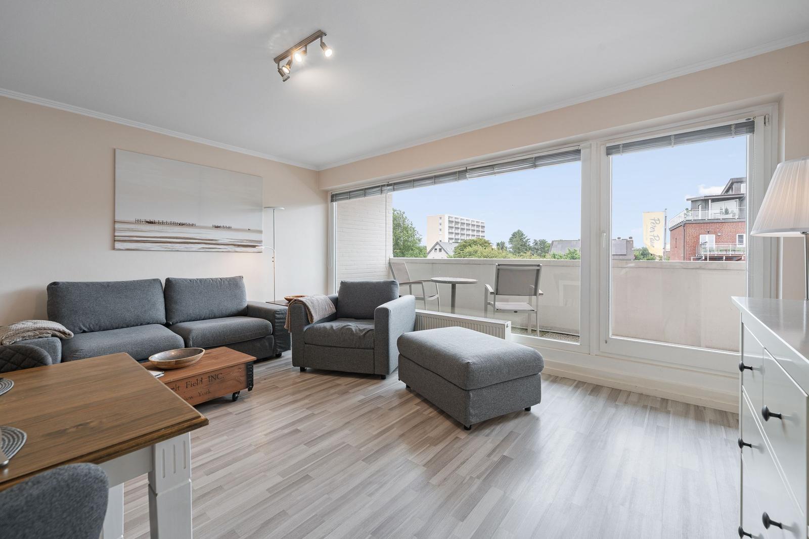 Wohnzimmer mit Sofa, Sessel und Balkon. Holzfußboden und große Fenster.