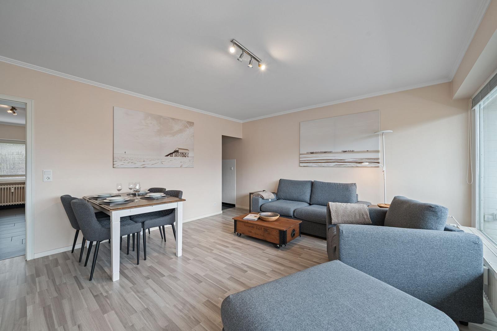 Wohn- und Essbereich mit grauem Sofa, Holztisch und Wandbildern.