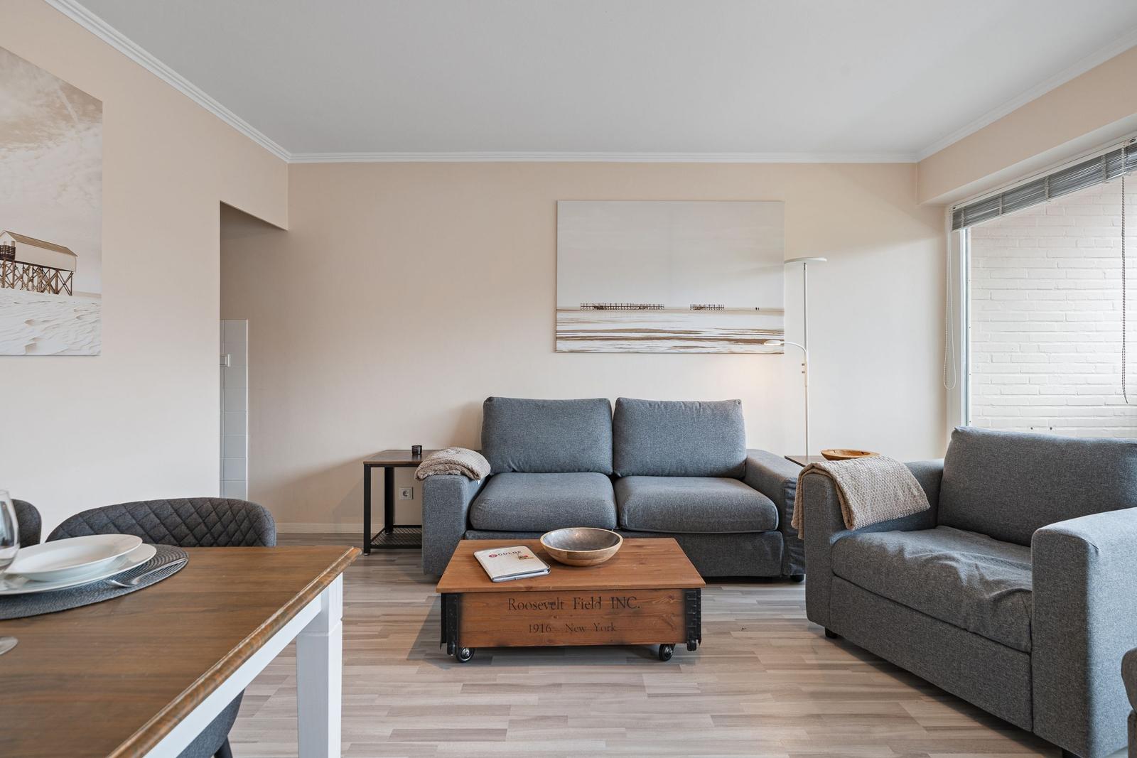 Wohn- und Essbereich mit grauem Sofa, Holztisch und Wandbildern.