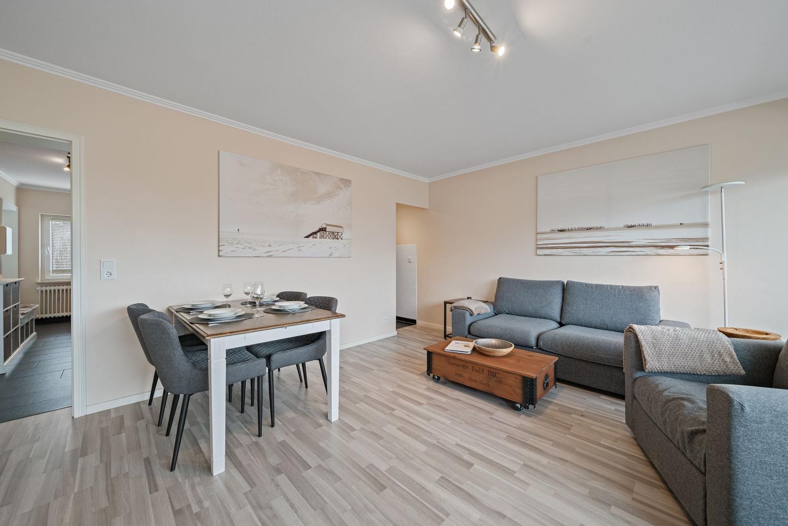 Wohn- und Essbereich mit grauem Sofa, Esstisch und Holzboden.