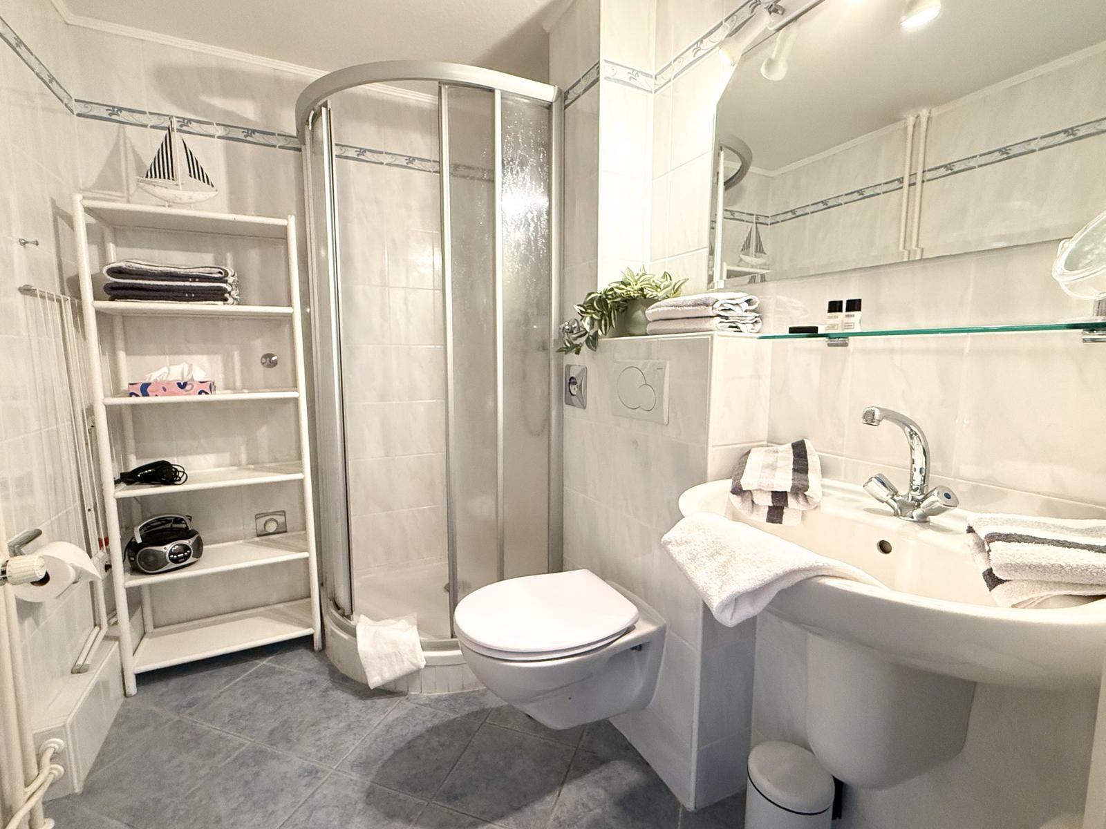 Bathroom with shower, sink, and toilet. Shelf with towels and decor.