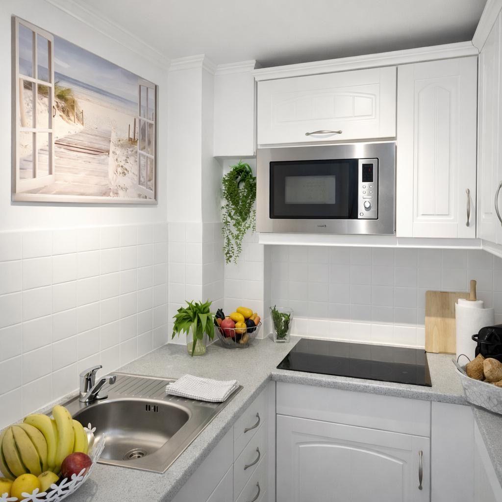 Kitchen with white built-in cabinets, stainless steel sink, and microwave. Wall picture shows beach.