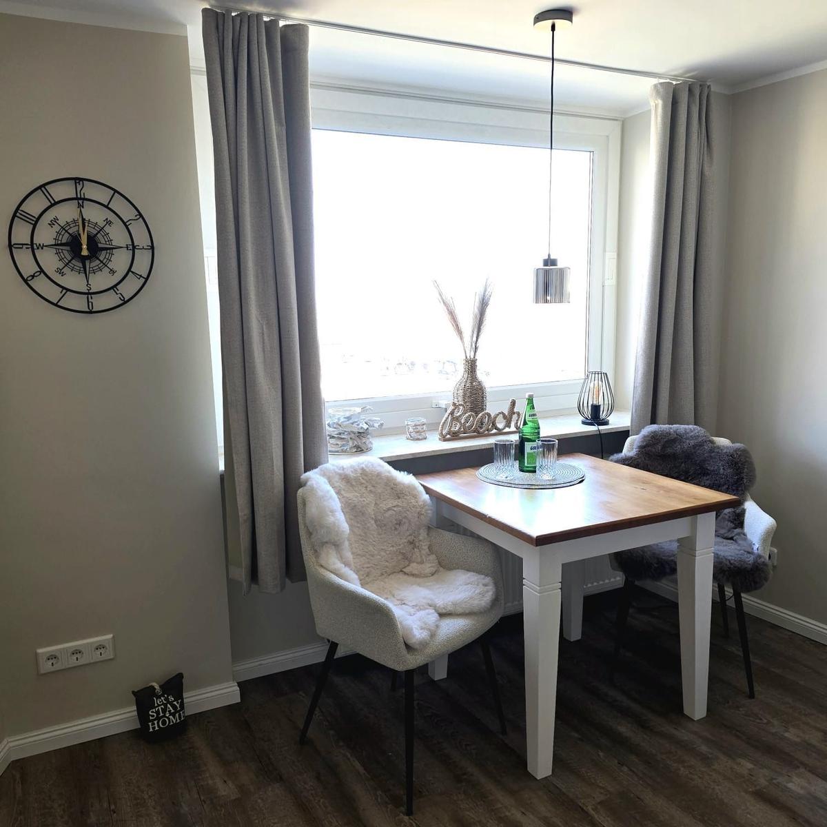 Dining area with table, two chairs, and window. Wall clock and curtains are visible.