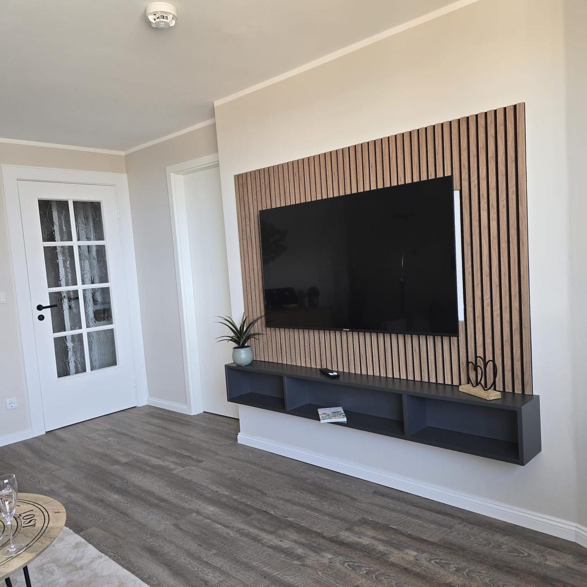 Living room with TV wall, wood paneling, and dark console. Wood floor and white walls.