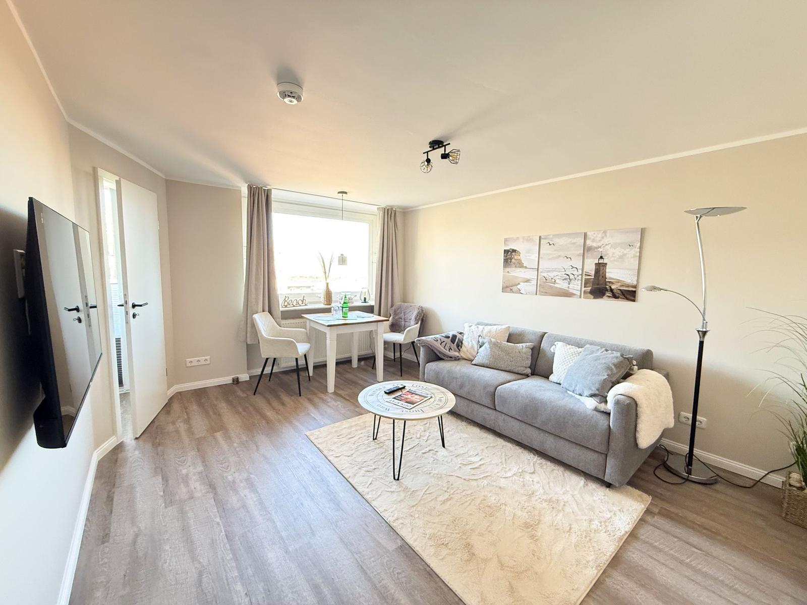 Living room with sofa, dining table, and TV. Window with curtains and wall art.
