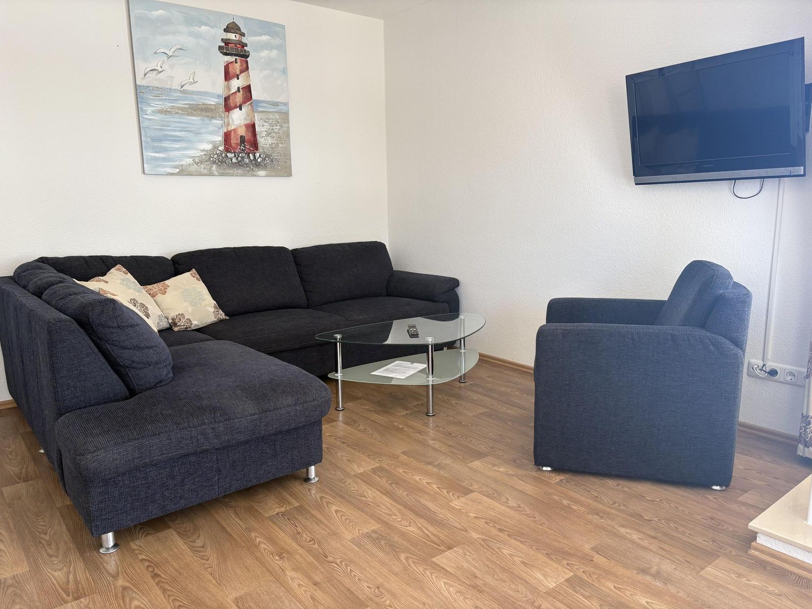 Wohnzimmer mit Sofa, Sessel, Glas-Tisch und Wandbild. Fernseher an der Wand.