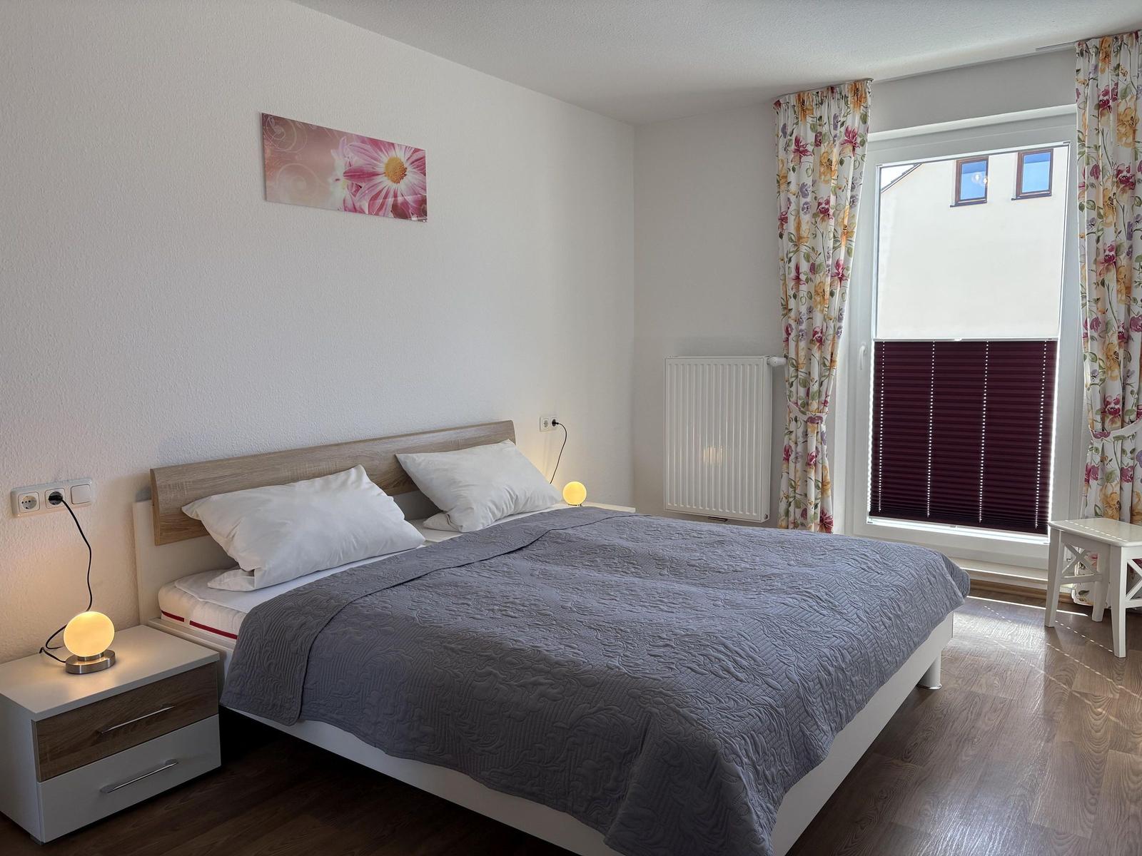 Schlafzimmer mit Doppelbett, Nachttisch und Fenster mit Blenden.