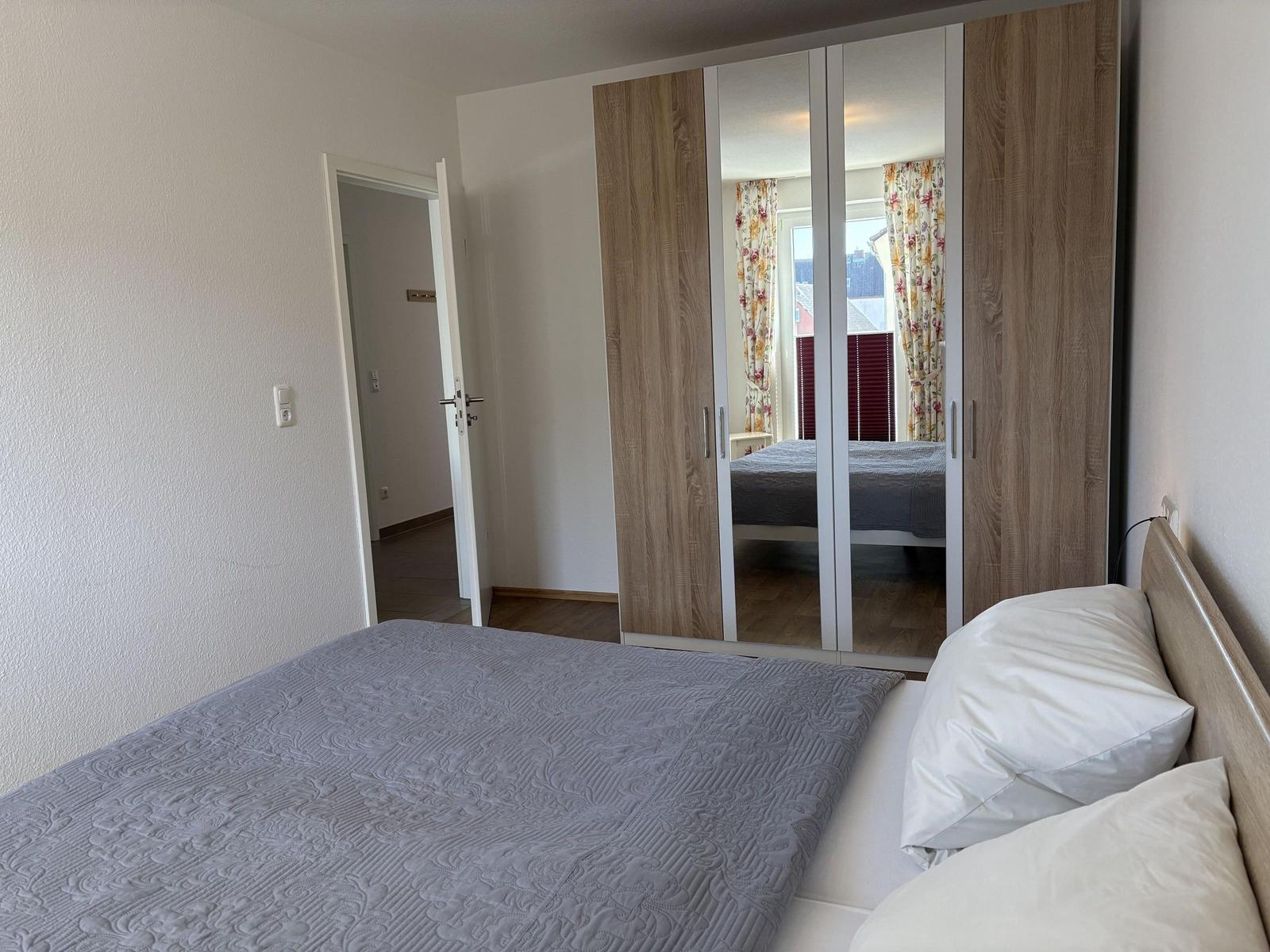 Schlafzimmer mit Bett, Spiegelschrank und Tür zum Flur.