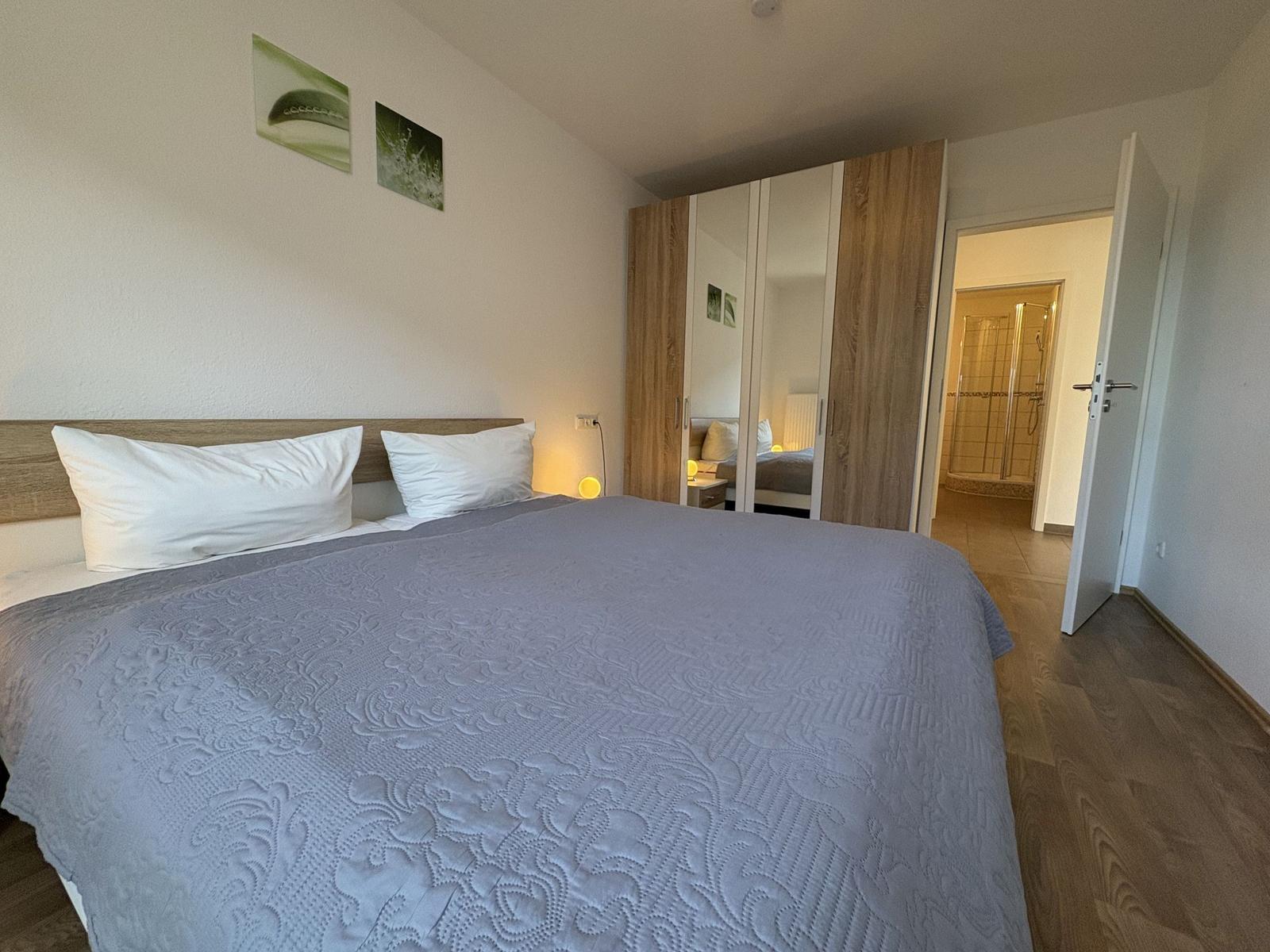 Schlafzimmer mit Doppelbett, Kleiderschrank und Blick in die Dusche.