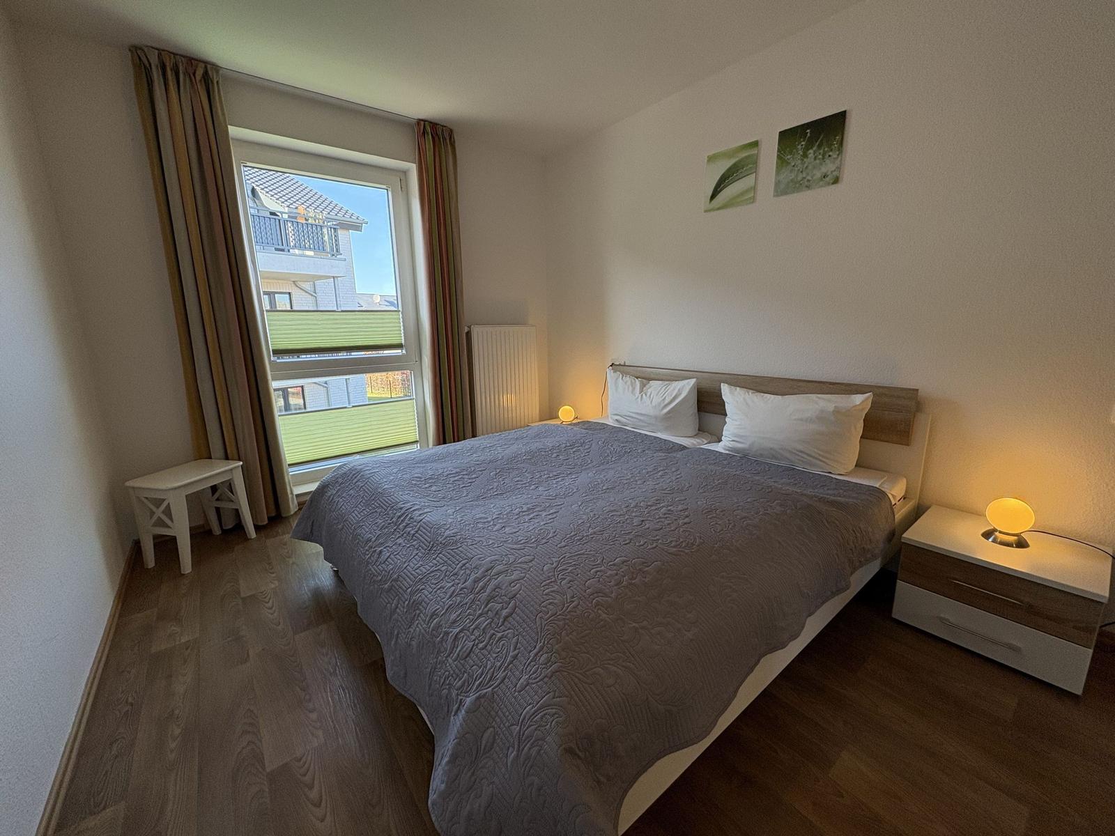 Schlafzimmer mit Doppelbett, Fenster und Nachttischen.
