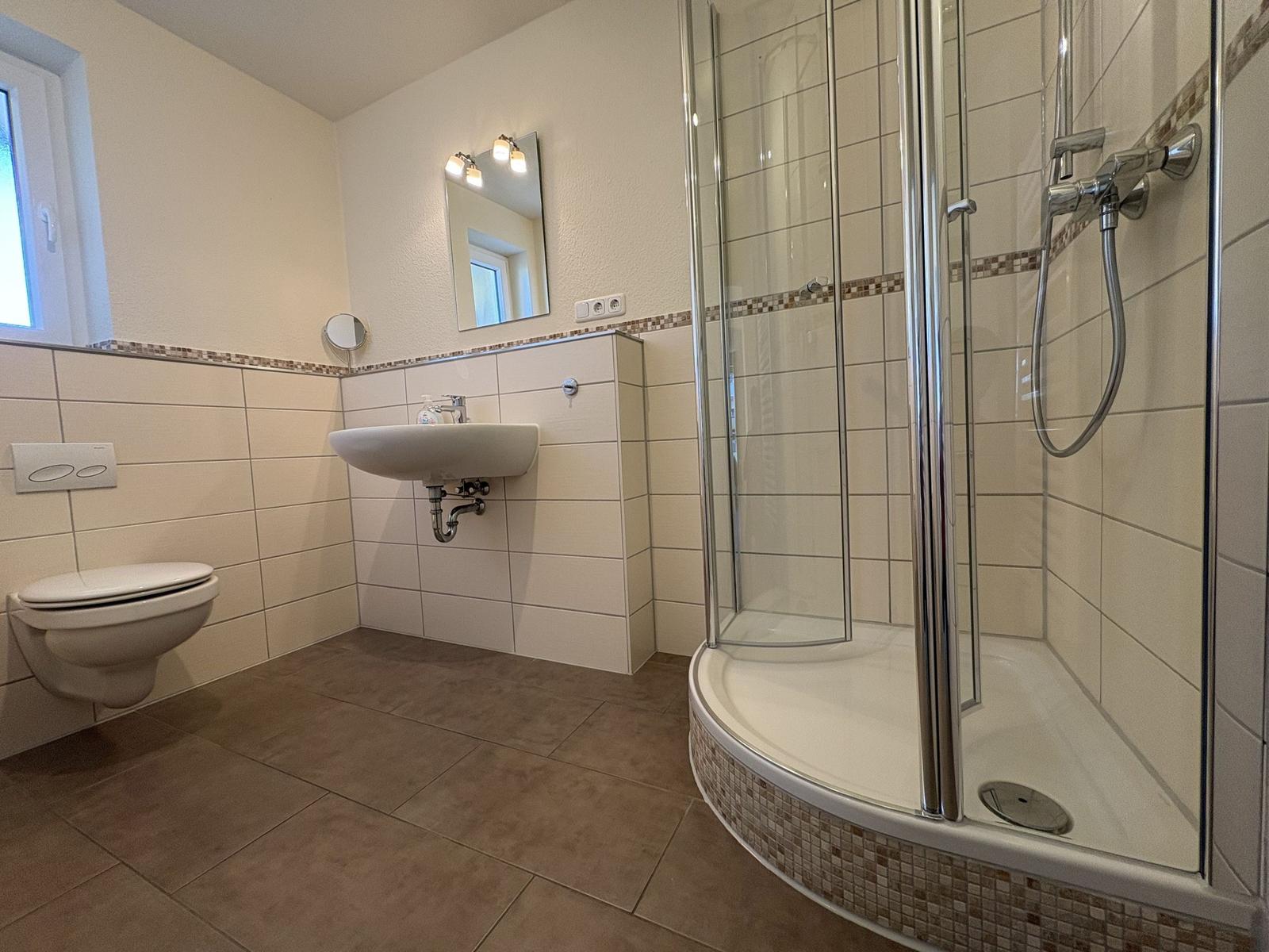 Bad mit Dusche, Waschbecken und WC. Fliesenwand und bodenfliesen.