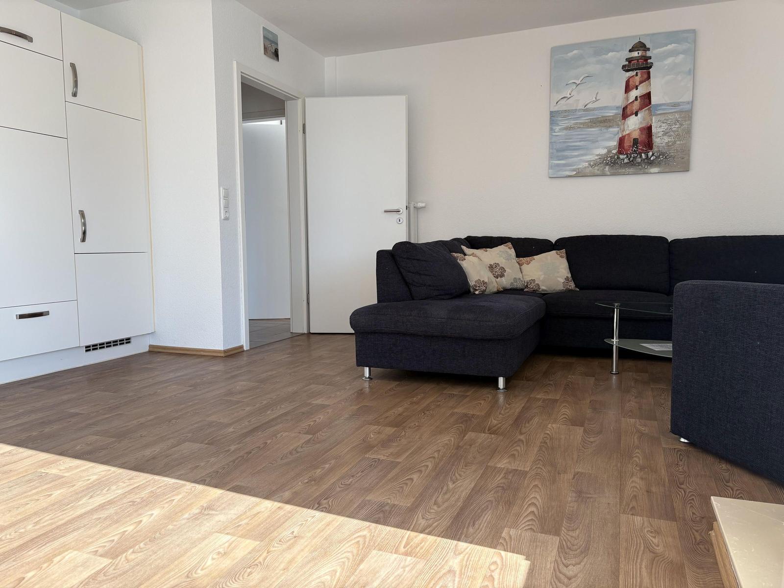Wohnzimmer mit Sofa, Holzboden und Leuchtturm-Bild an der Wand.