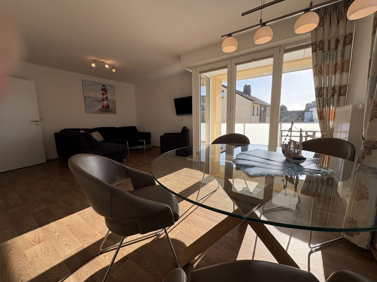 Essbereich mit Glas-Tisch und Stühlen. Wohnzimmer mit Sofa und Fernseher. Blick auf Balkon.