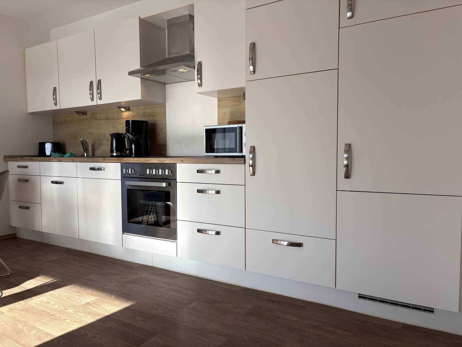 Moderne Küche mit weißen Schränken, Edelstahlgeräten und Holz Arbeitsplatte.