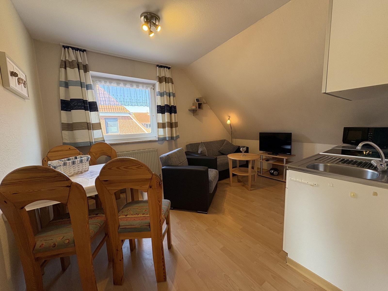 Wohnküche mit Essbereich, Sofa, TV und Fenster mit Blick auf Dach.
