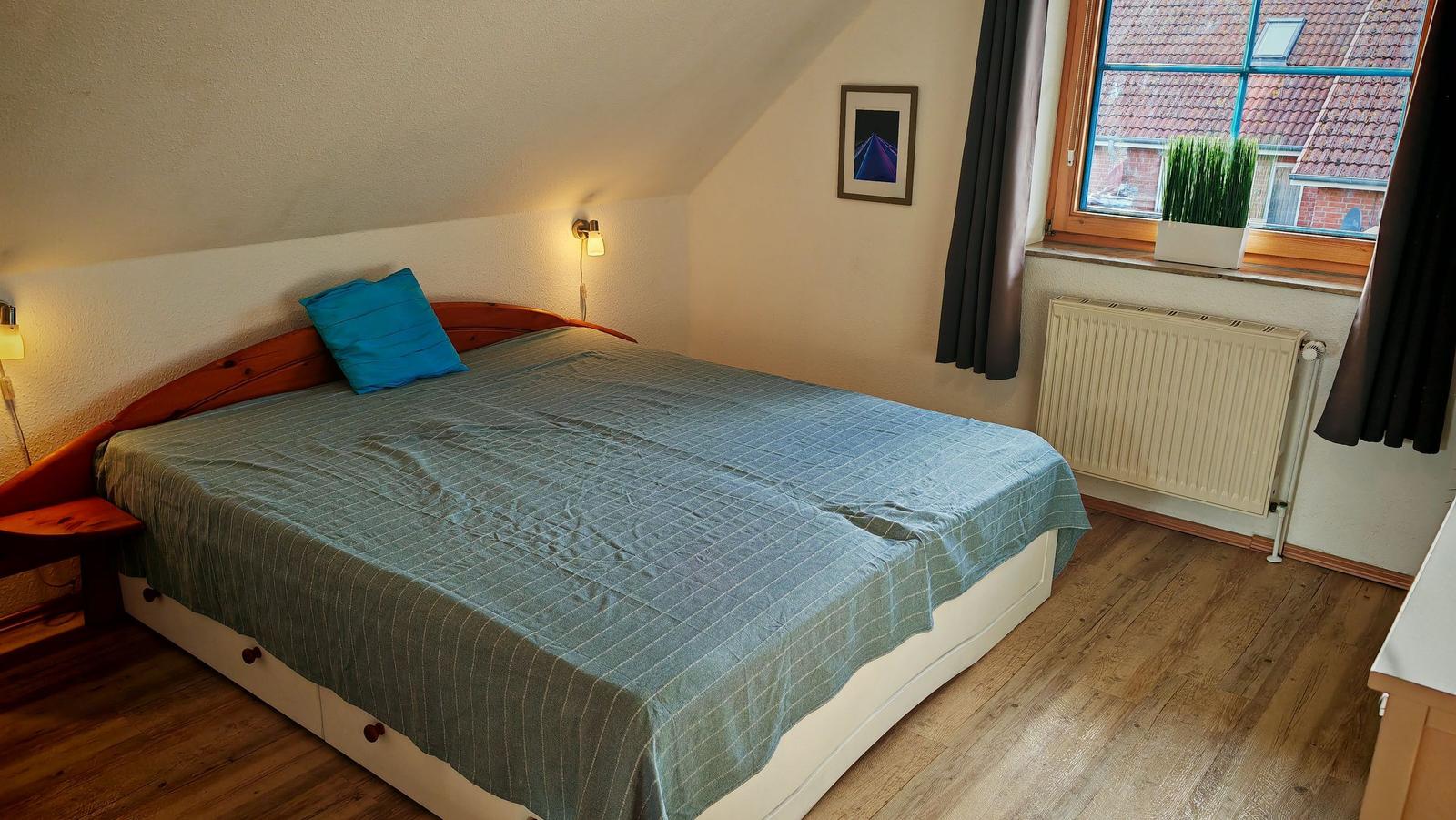Schlafzimmer mit Doppelbett, Holzboden und Fenster mit Blick auf Dach