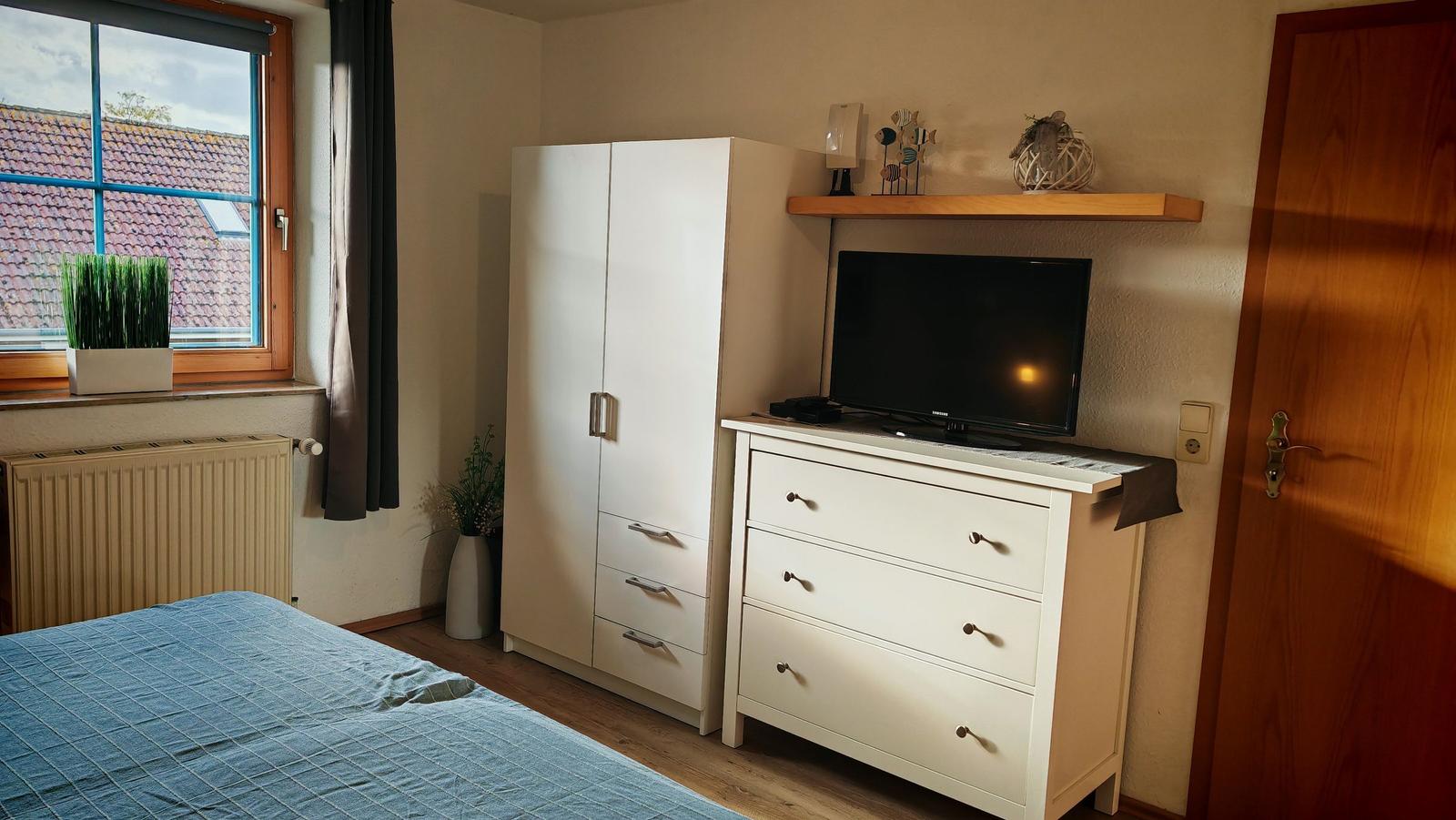 Schlafzimmer mit Bett, Kleiderschrank und TV-Schrank. Fenster mit Blick auf Dach.