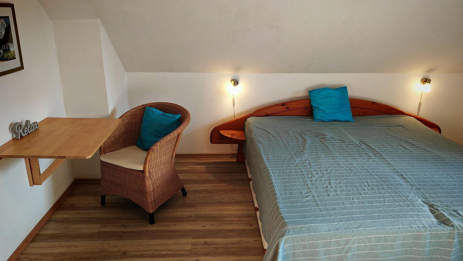 Schlafzimmer mit Bett, Wickerstuhl und Schreibtisch an der Wand.