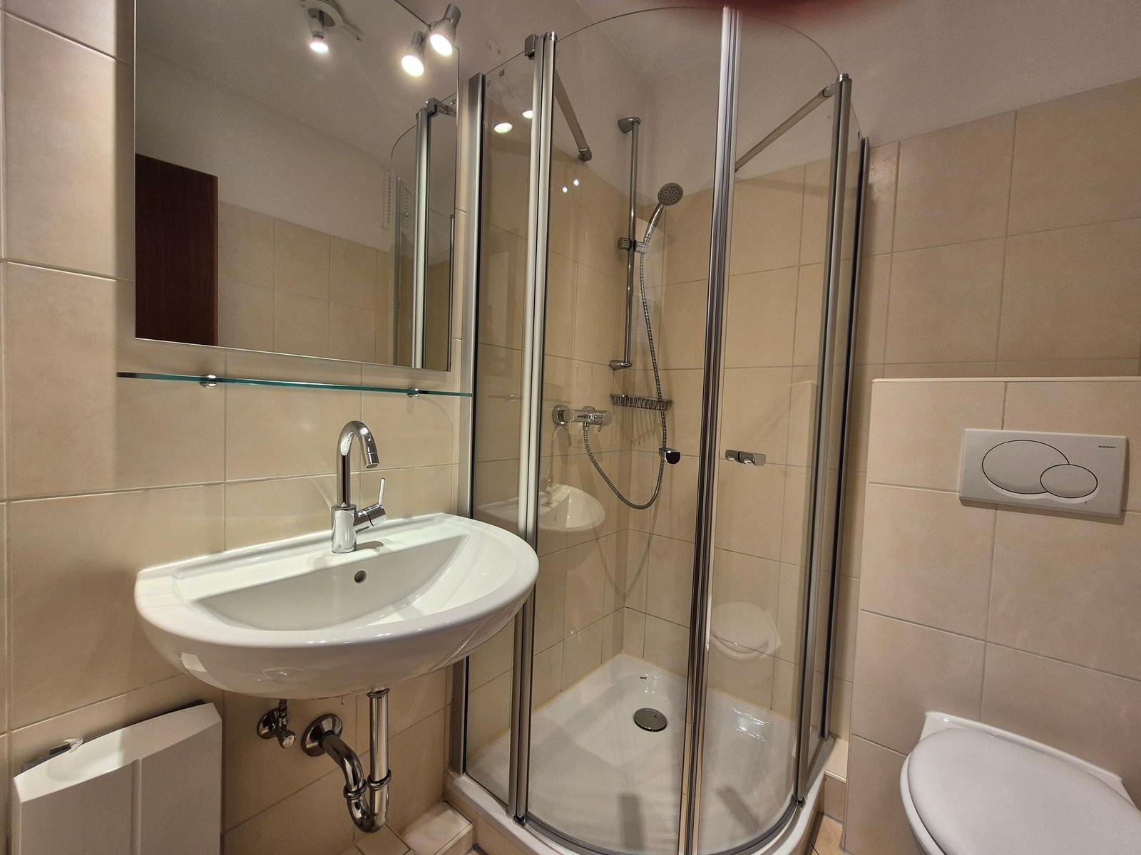 Badezimmer mit Dusche, Waschbecken und Toilette. Fliesenwand und Spiegel.