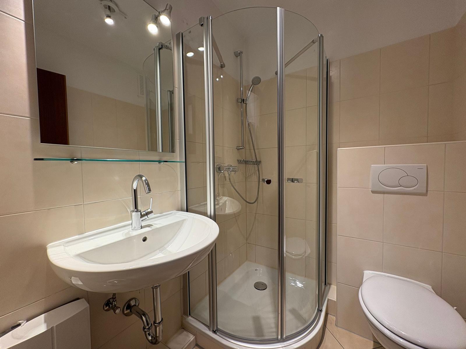 Badezimmer mit Dusche, Waschbecken und Toilette. Fliesenwand und Spiegel.