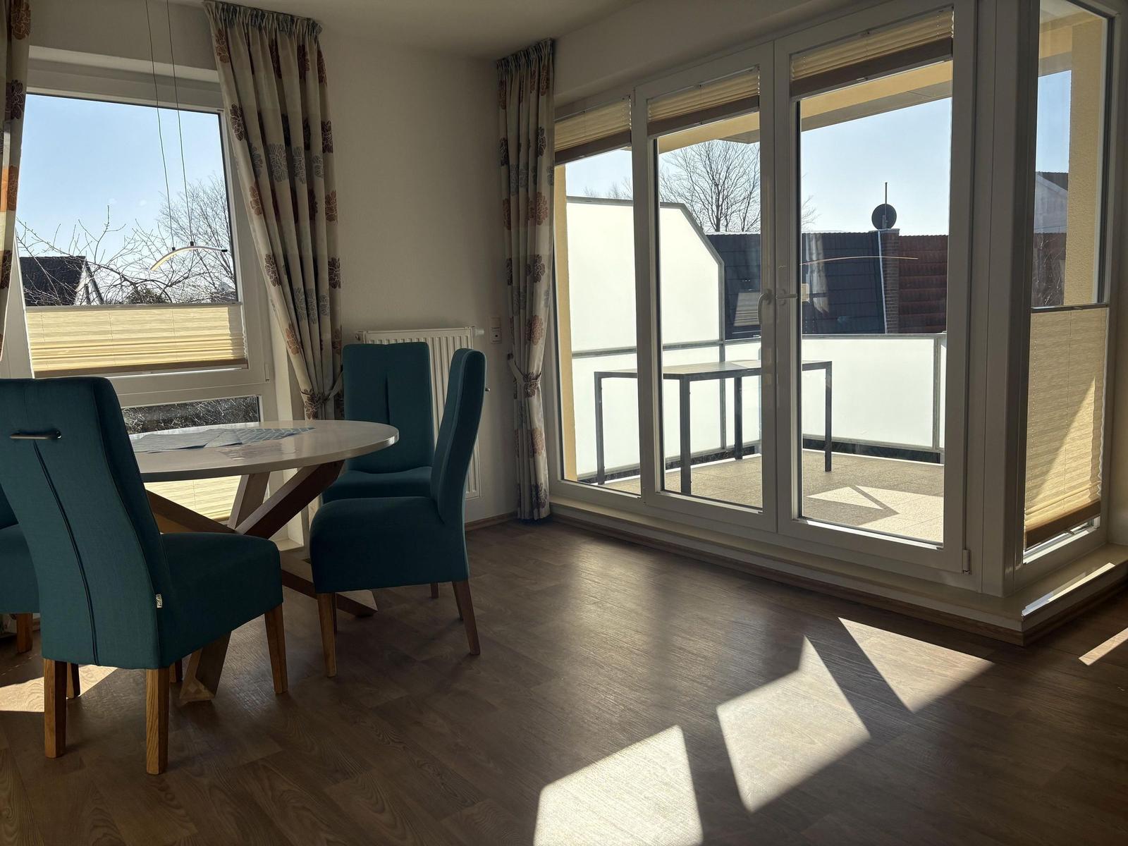 Essbereich mit Tisch und Stühlen, große Fenster und Balkon mit Tisch.