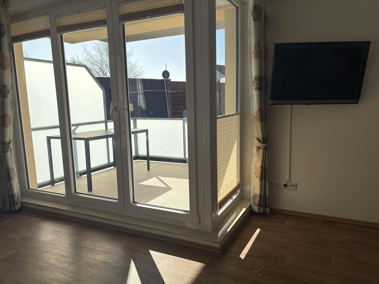 Raum mit bodentiefen Fenstern, Balkon und Wandfernseher.