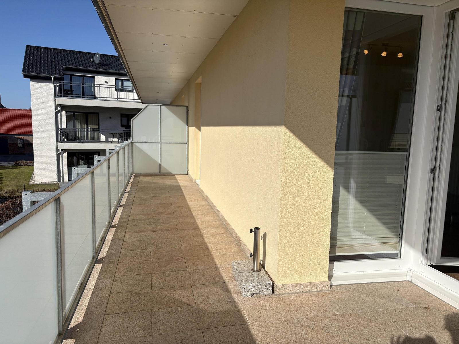 Gelber Balkon mit Glasgeländer und Terrassenplatte. Tür führt ins Haus.