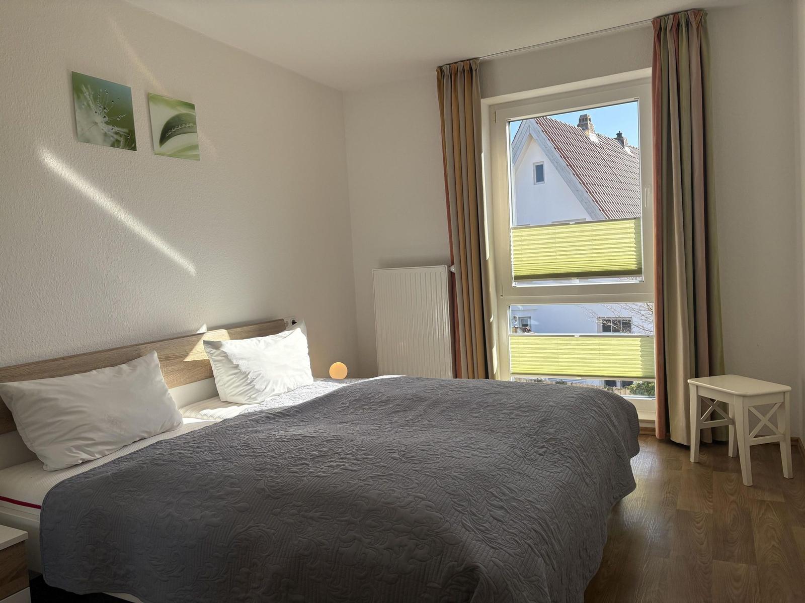 Schlafzimmer mit Bett, Fenster und Holzboden. An der Wand hängen zwei Bilder.