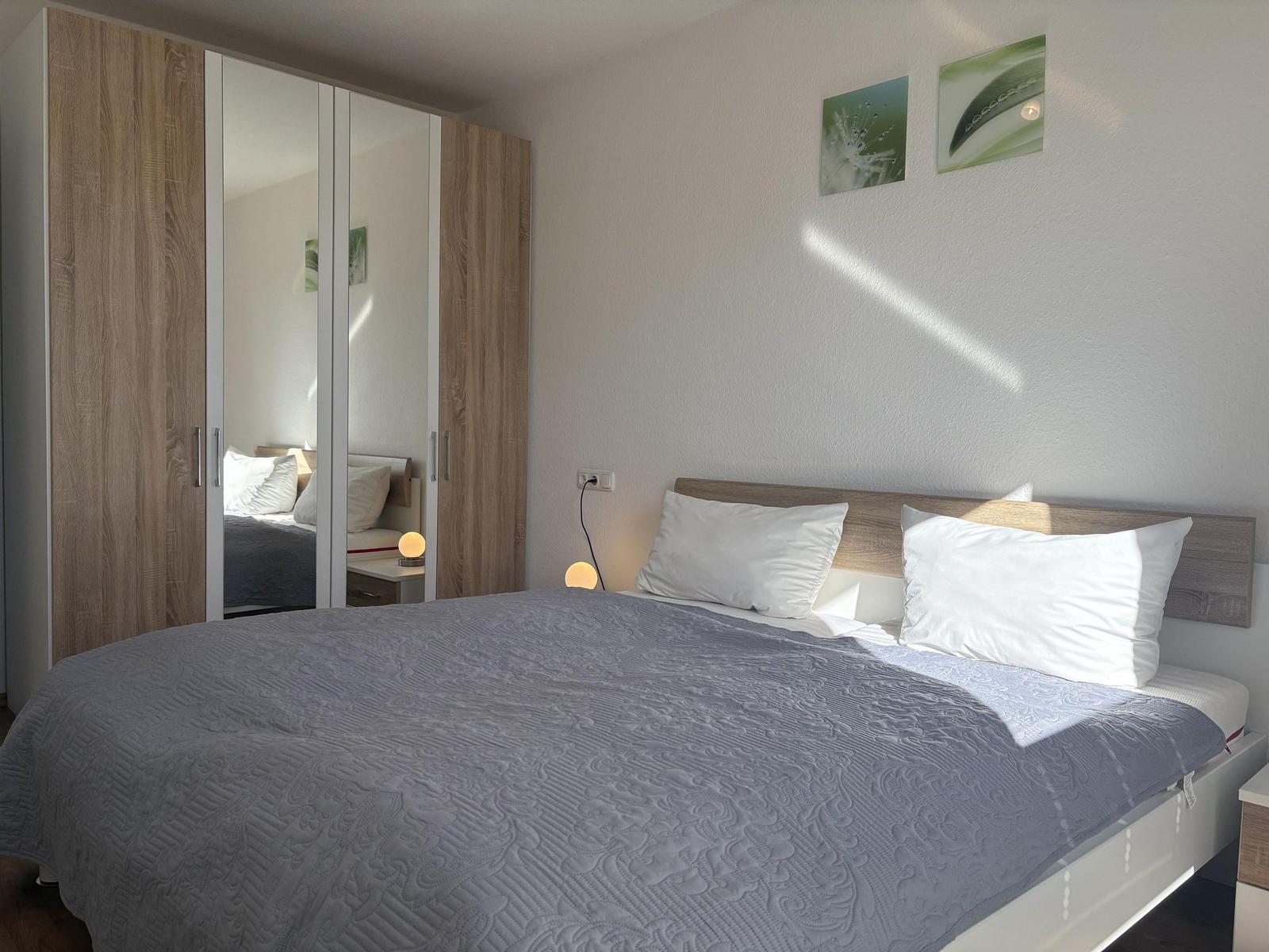 Schlafzimmer mit Doppelbett, Kleiderschrank mit Spiegeltüren und Wandbildern.