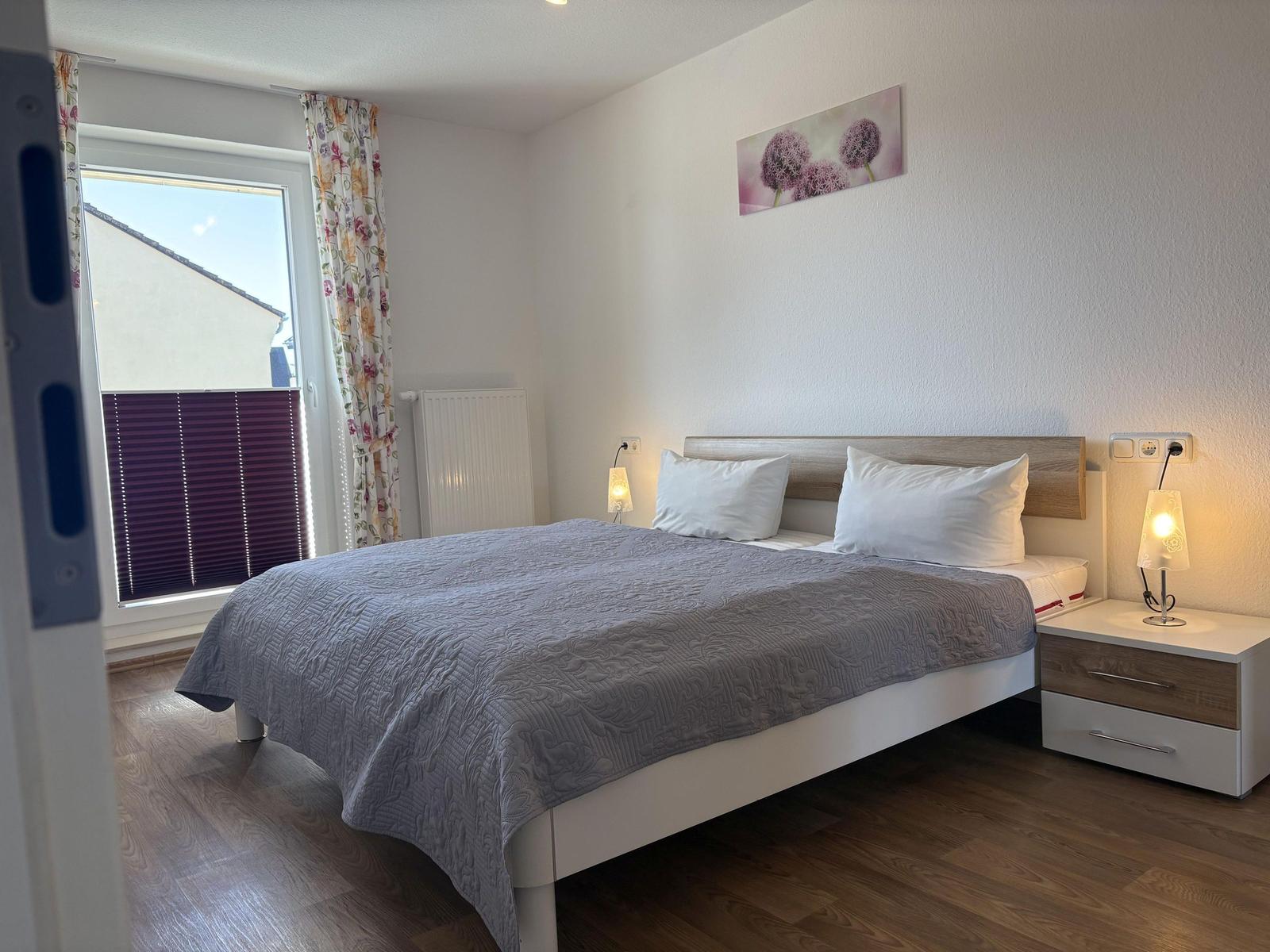 Schlafzimmer mit Doppelbett, Nachttisch und Fenster mit Vorhängen.