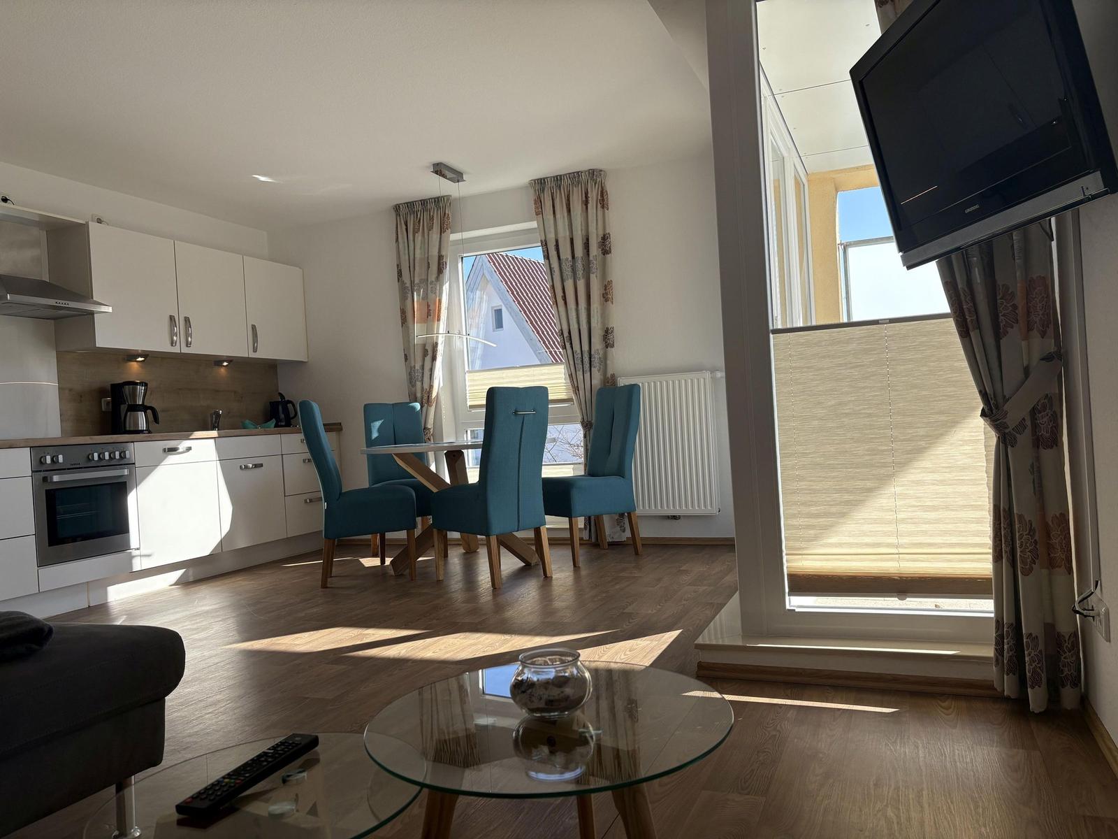 Wohnküche mit Esstisch, vier Stühlen und Balkon. Fernseher an der Wand.