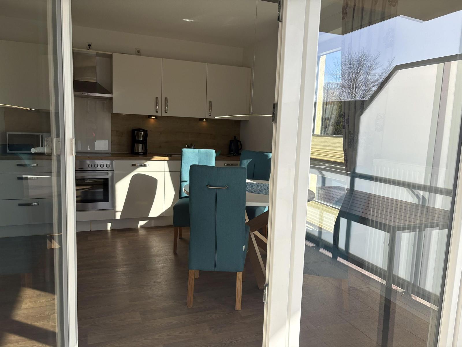 Küche mit Essbereich und Balkon. Blaue Stühle, weiße Schränke, Holzboden.