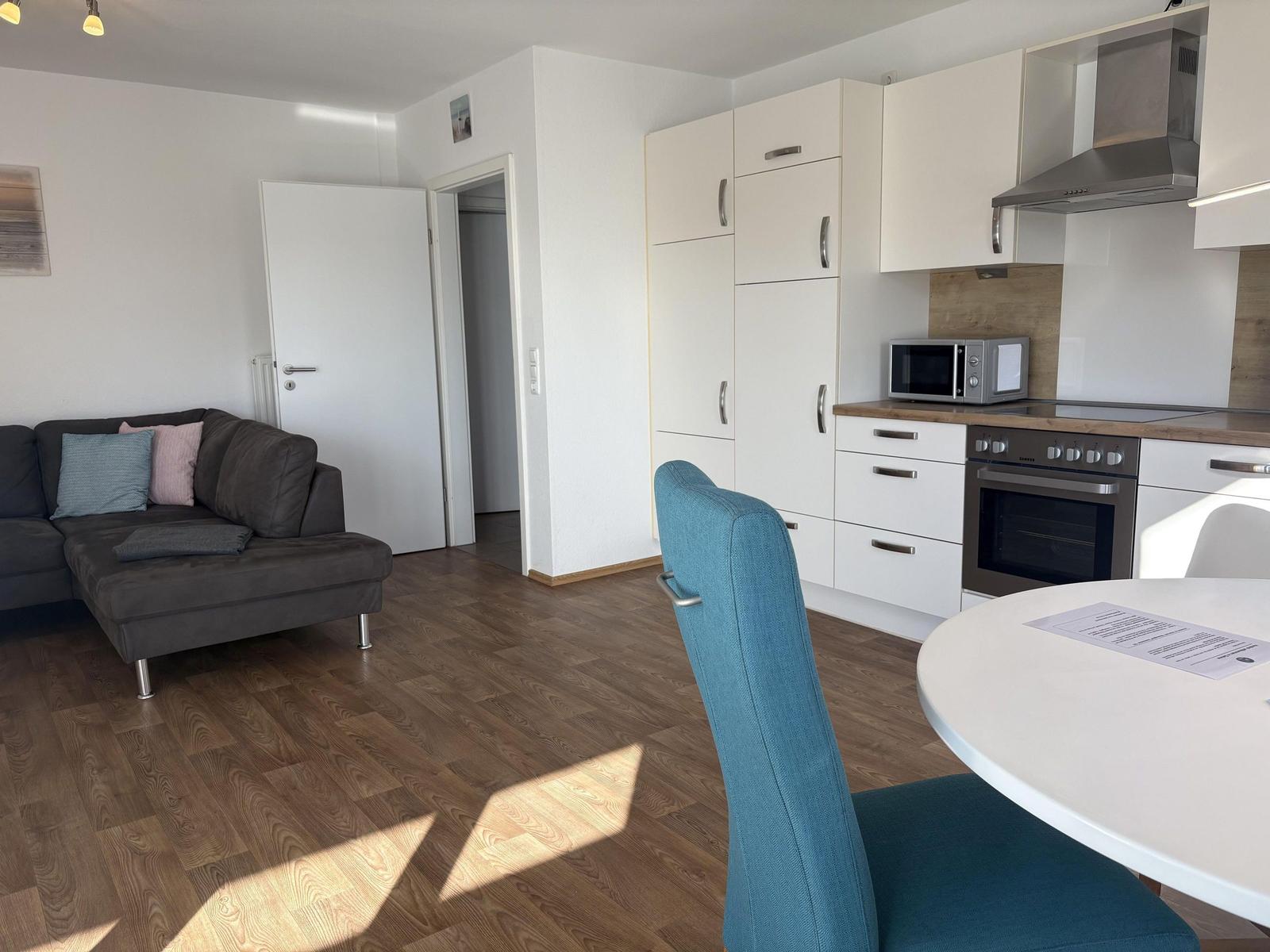 Wohn- und Küchenbereich mit Sofa, Esstisch und weißen Schränken.