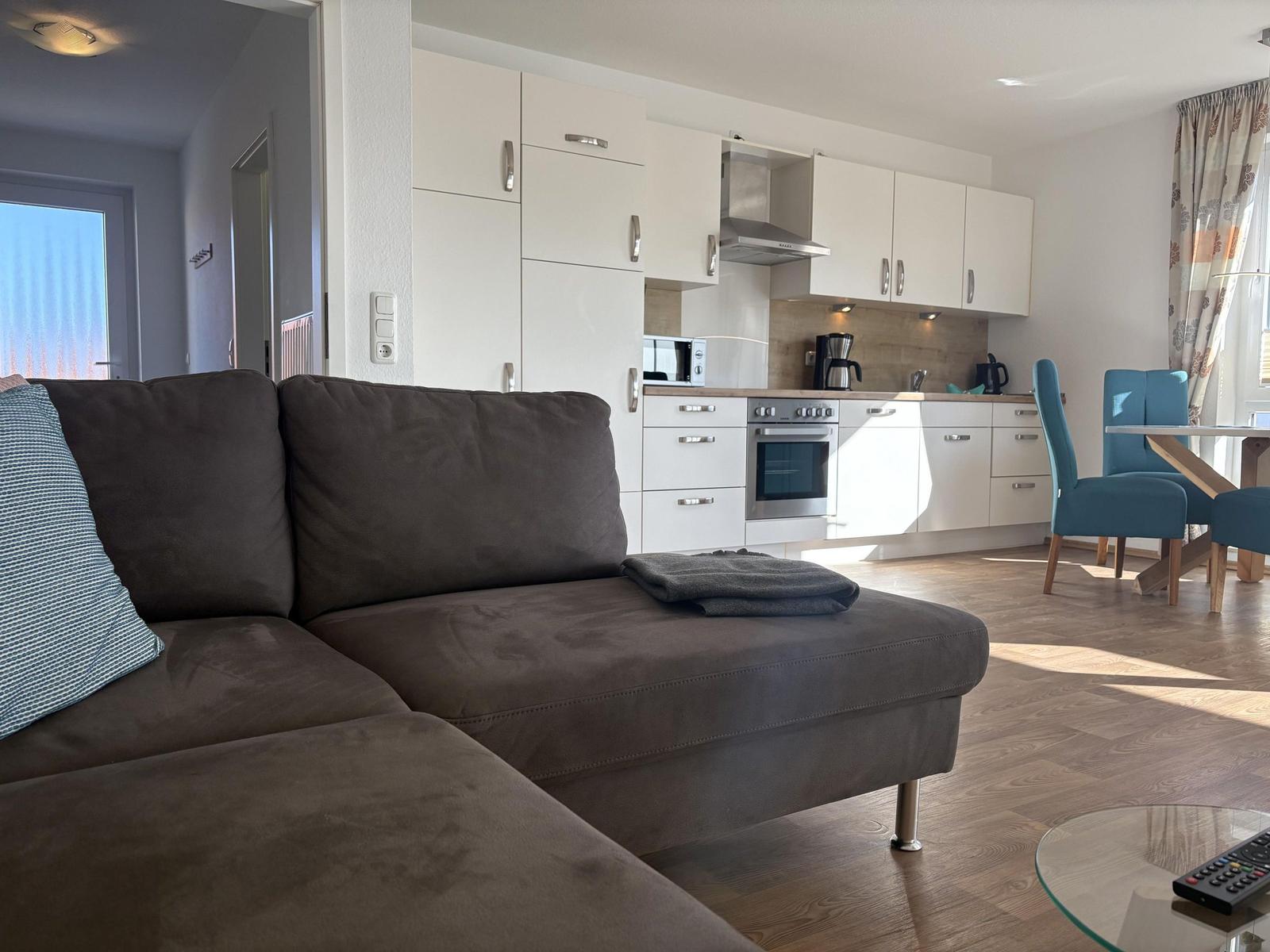 Wohnbereich mit Sofa, Küche und Essplatz. Holzboden und weiße Schränke.