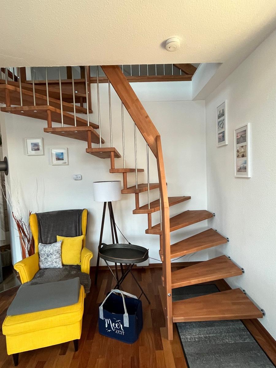 Holztreppe führt zur oberen Etage. Gelber Sessel und Beistelltisch im Vordergrund.