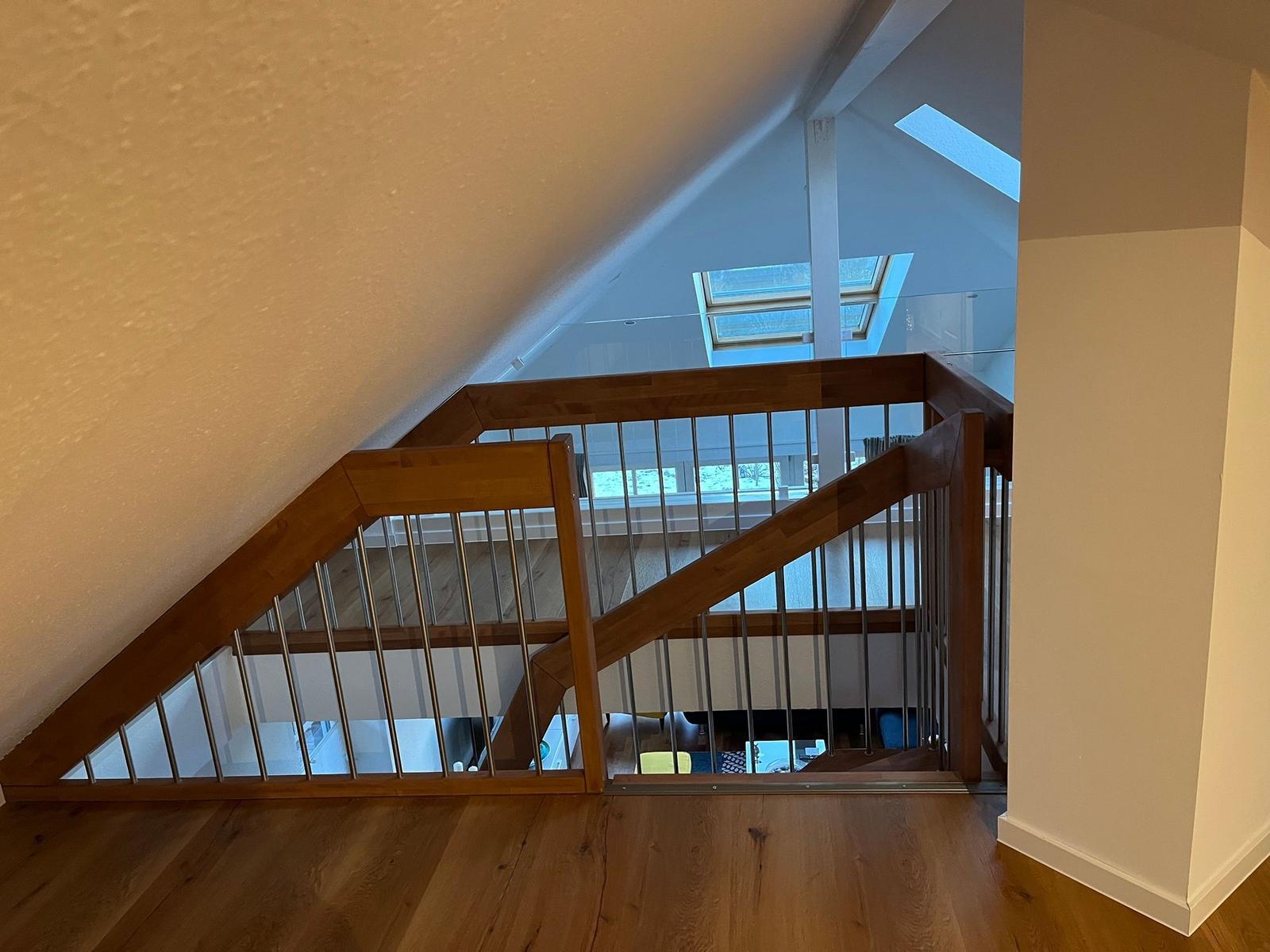 Holzgetreppe mit Metallgeländer führt zu einer hohen Decke mit Dachfenstern.