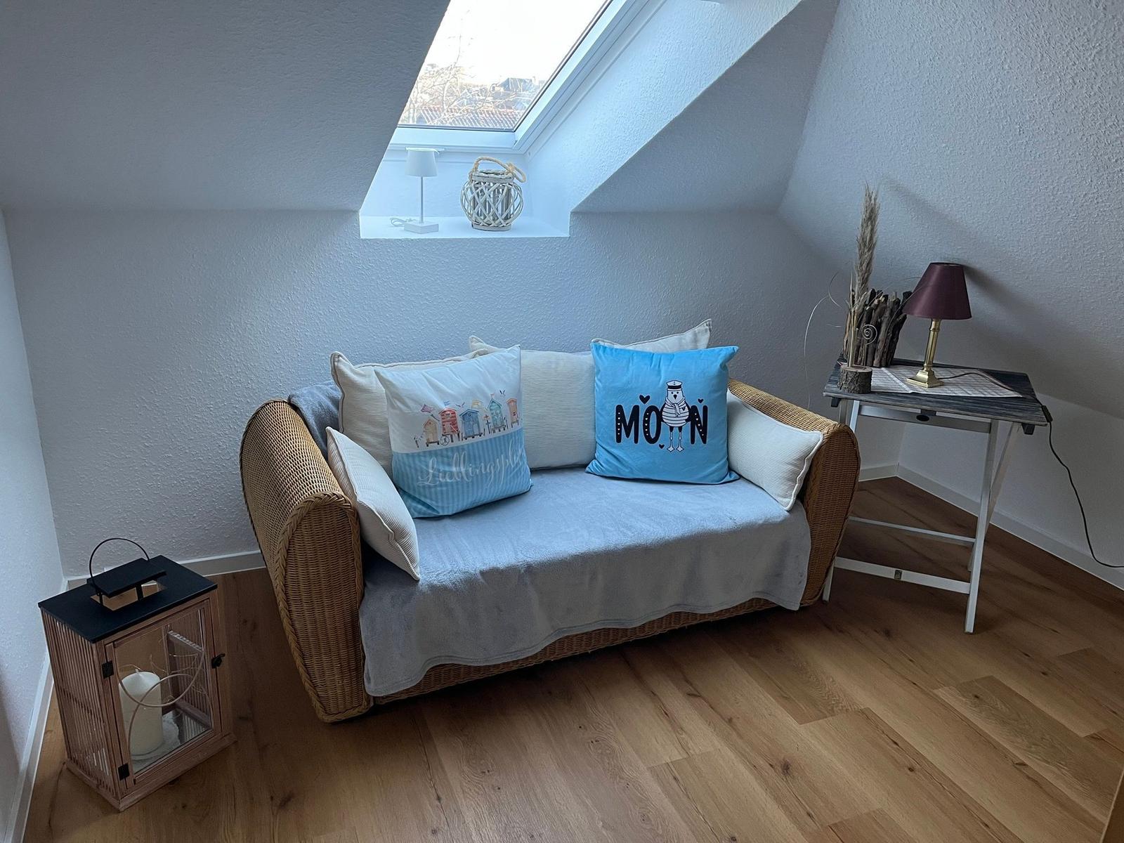 Ein Schlafzimmer mit Dachschräge, Sofa, Tisch und Fenster. Holzfußboden und weiße Wände.