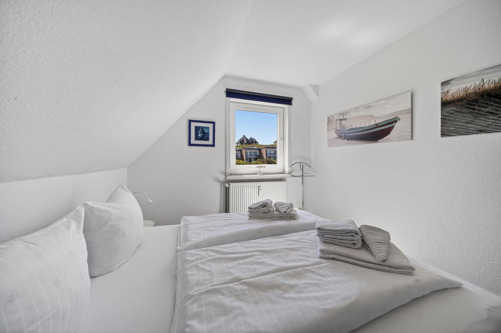 Schlafzimmer mit Dachschrägen, Bett, Fenster und Wandbildern.