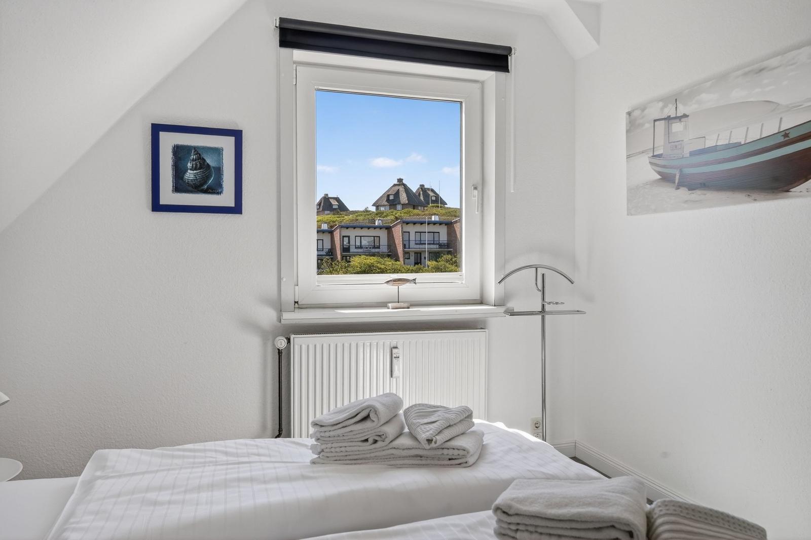Schlafzimmer mit Blick auf Häuser und Himmel. Bett mit Handtüchern. Wandbild und Fenster.
