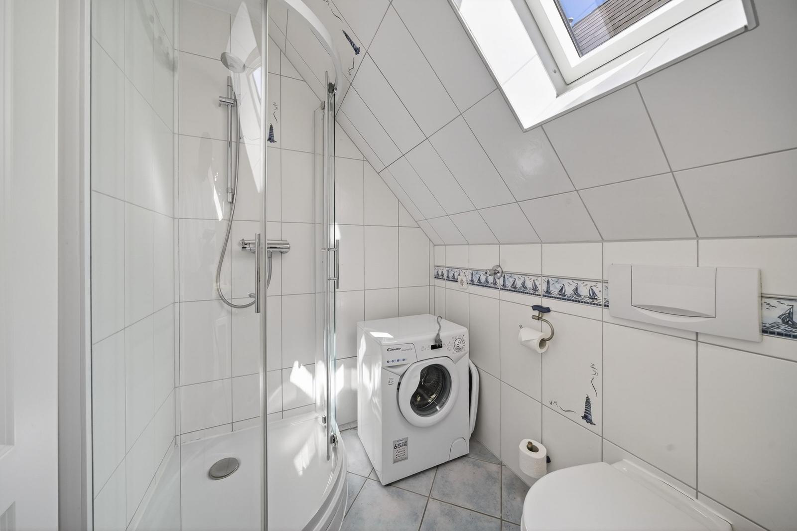Badezimmer mit Dusche, Waschmaschine und Toilette unter Dachschrägen mit Dachfenster.