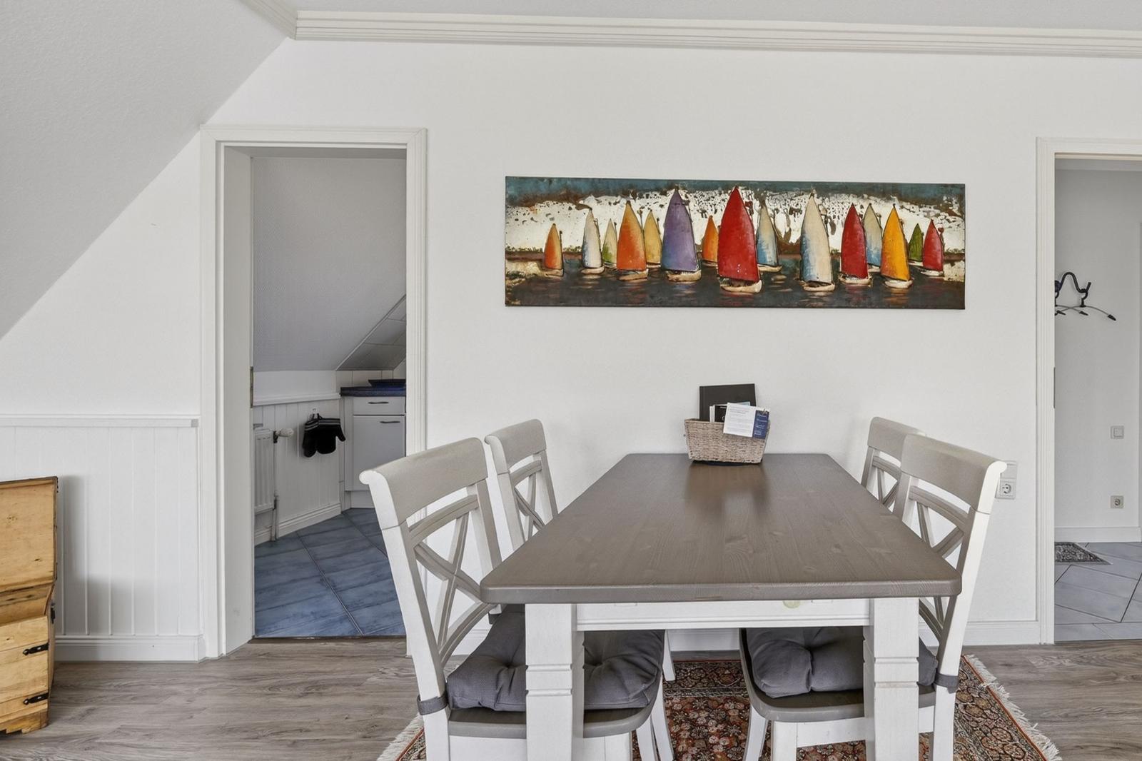 Esszimmer mit Tisch, Stühlen und Wandbild mit Segelbooten.