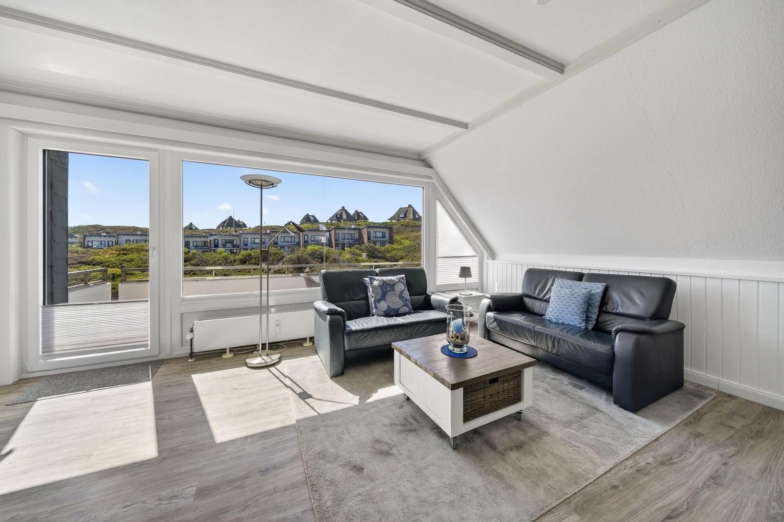 Wohnzimmer mit zwei schwarzen Sofas, Tisch und Blick auf Wohnhäuser.