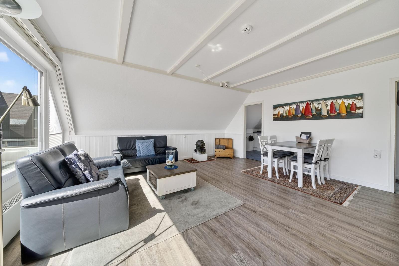 Wohn- und Essbereich mit Sofa, Tisch und Fenster. Decke mit Holzverkleidung.