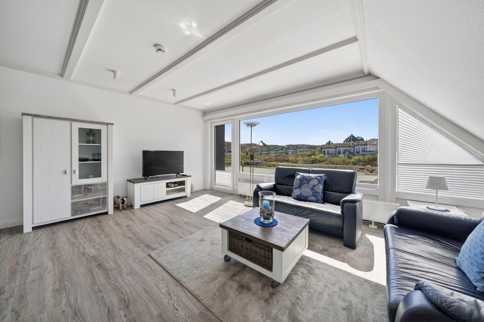 Wohnzimmer mit Sofa, Fernseher und Blick auf die Landschaft.
