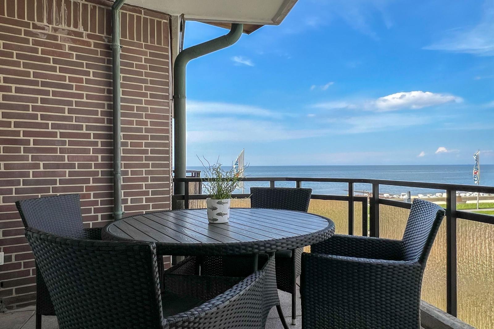 Terrasse mit Tisch und Stühlen, Blick auf Meer und Strand.
