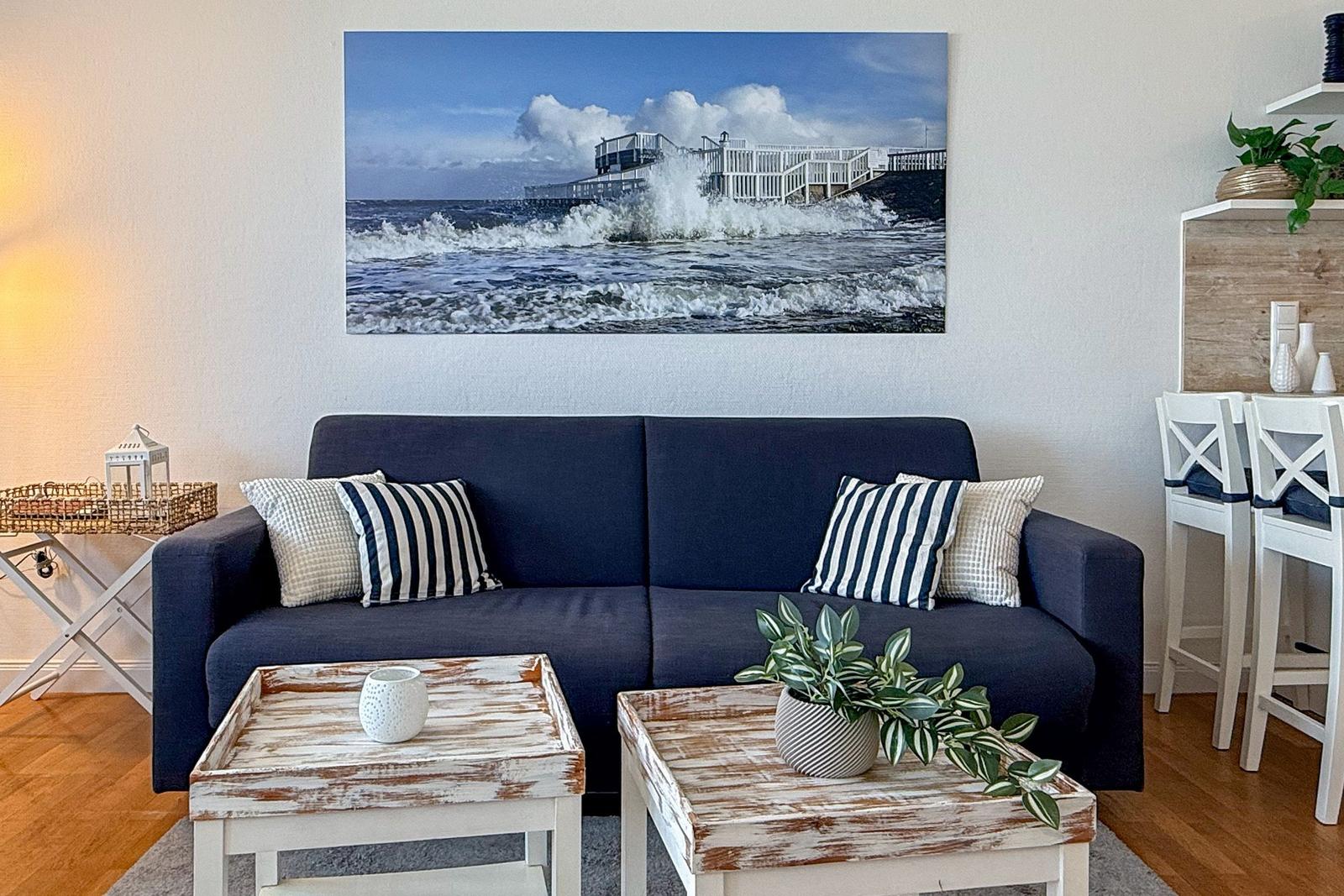 Ein Wohnzimmer mit dunkelblauem Sofa, zwei rustikalen Tischen und einer Wanddekoration mit Meeresszene.