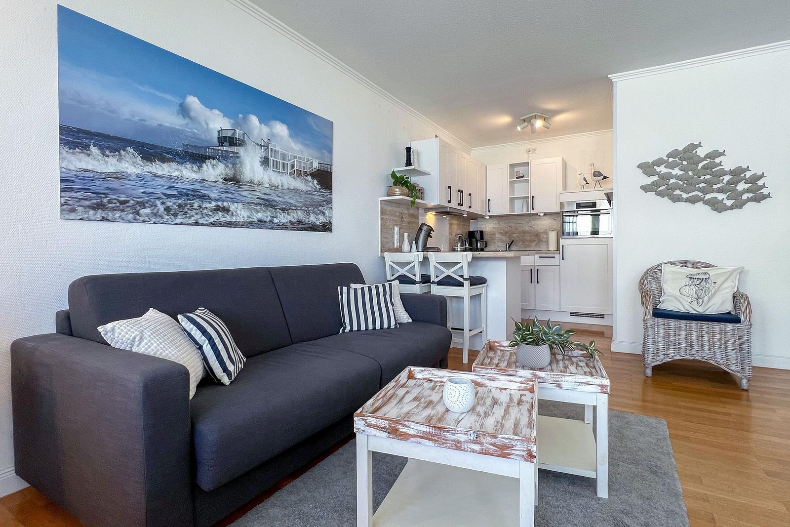 Wohnzimmer mit Sofa, Couchtisch und Küchenbereich. Wandbild und Sitzgelegenheit sichtbar.