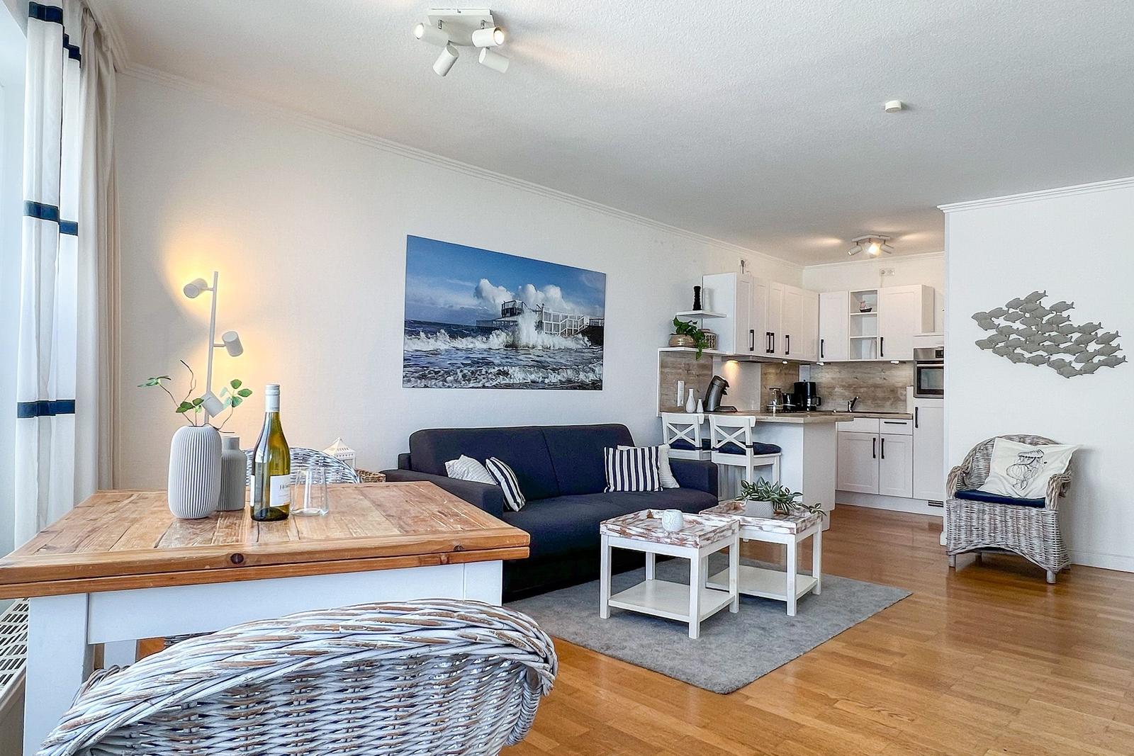 Wohnzimmer mit Sofa, Esstisch und Küche im Hintergrund.