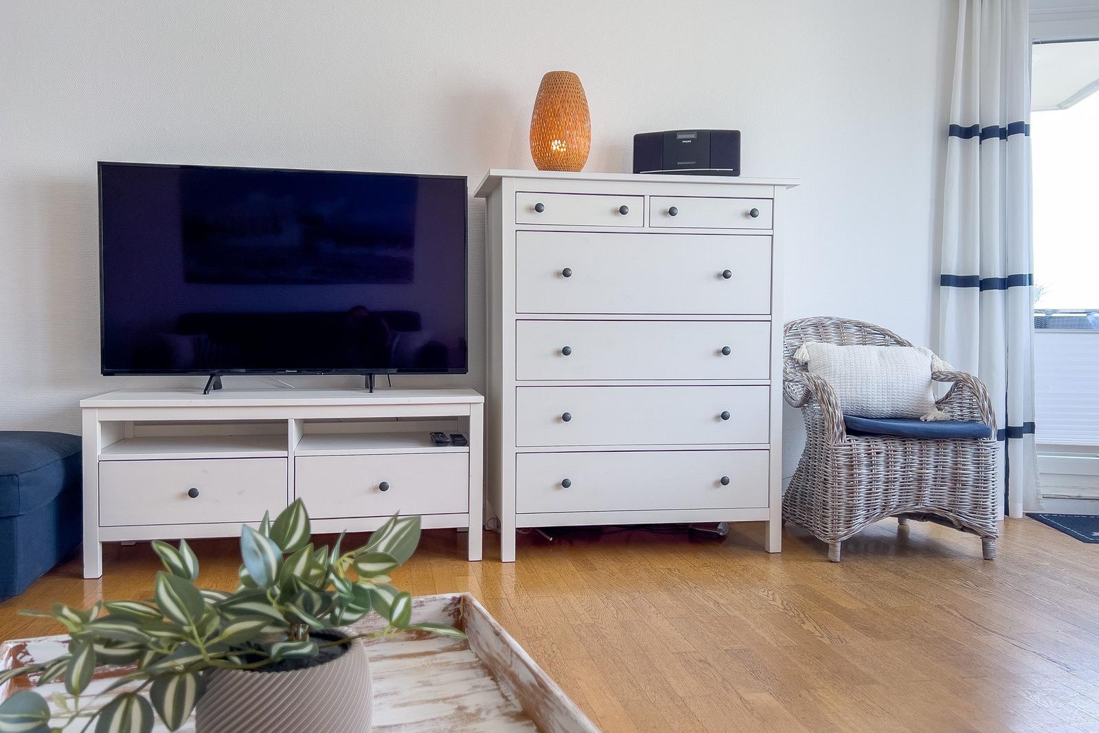 Wohnzimmer mit Fernseher, Schrank und Stuhl vor Fenster