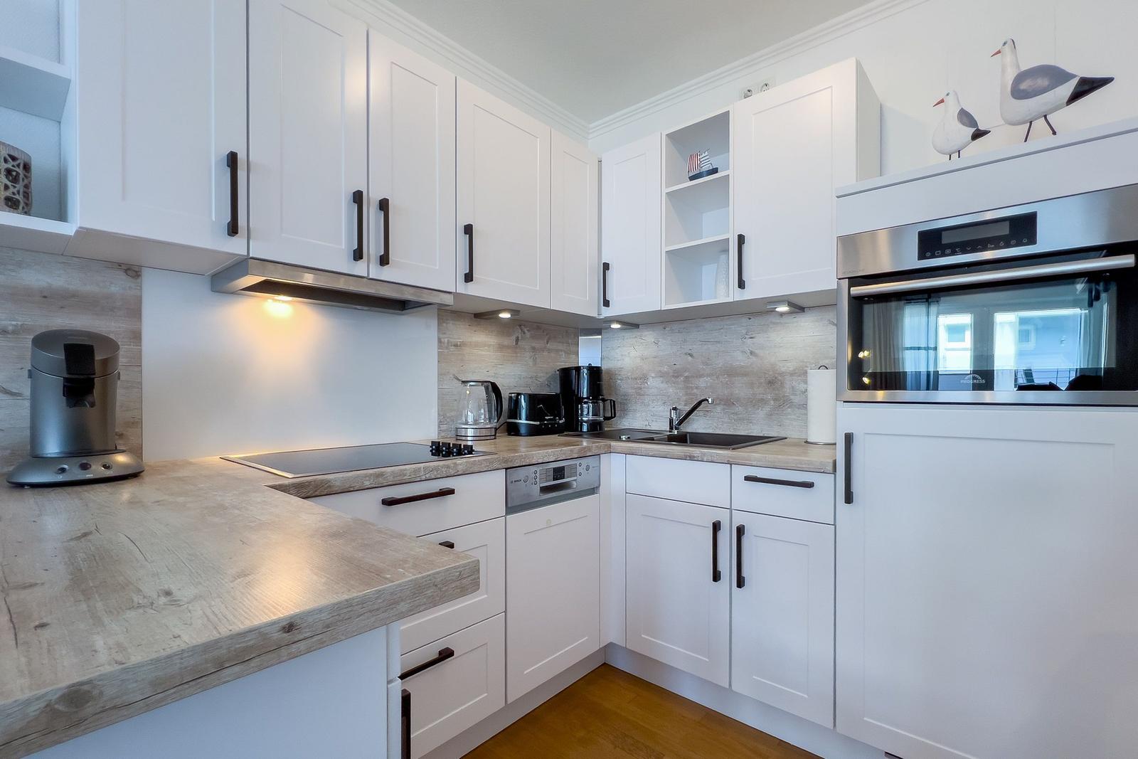 Moderne Küche mit weißen Schränken, Holzoberflächen und integriertem Backofen.